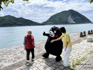 三角西港で笑顔でお話しする観光ガイドさんとくまモン、アナウンサー